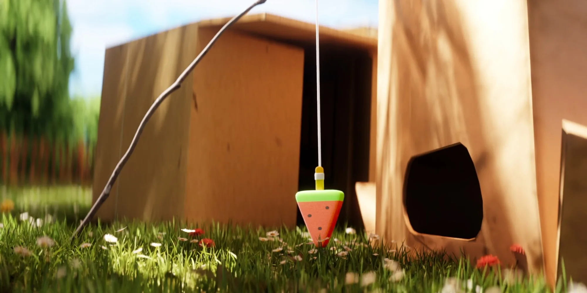 A watermelon-slice toy dangles from a stick and string in the grass beside cardboard boxes.